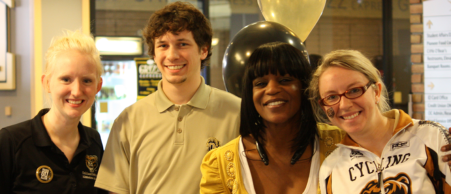 four people wearing black, white and gold in an office with balloons behind them
