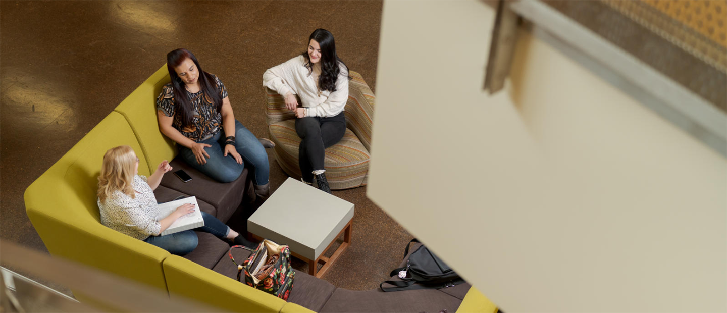 An aerial photo of three women seated on a couch, in conversation.