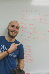man in a blue O U W B t-shirt pointing to writing on a white board