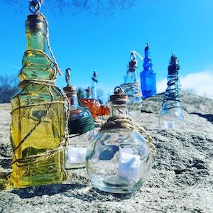 Field art, multi-colored glass bottles, some wrapped with twine, outside on rocks