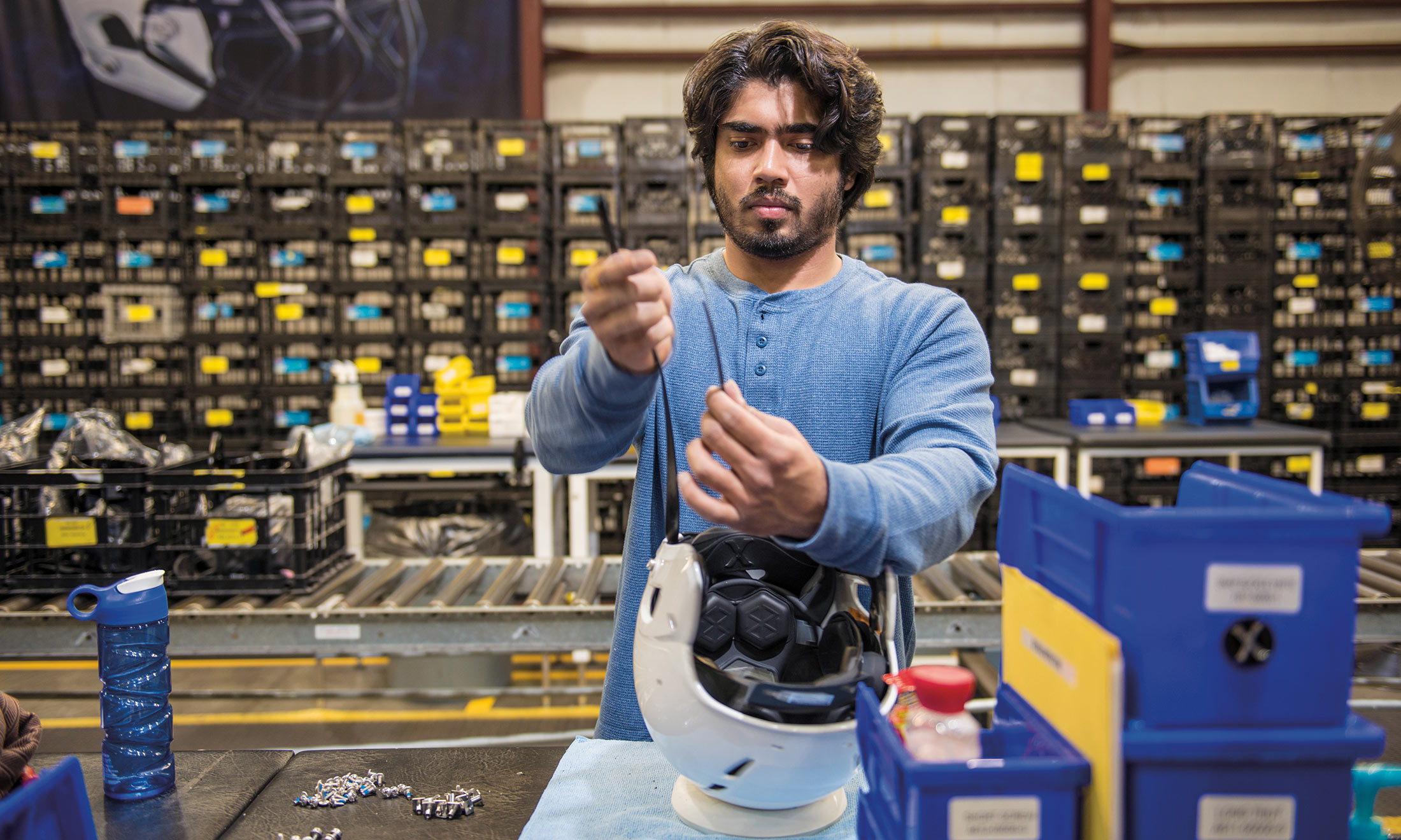 Oakland University grad student Prateek Bansal fastens a chin strap to a white helmet at a Xenith production factory in downtown Detroit
