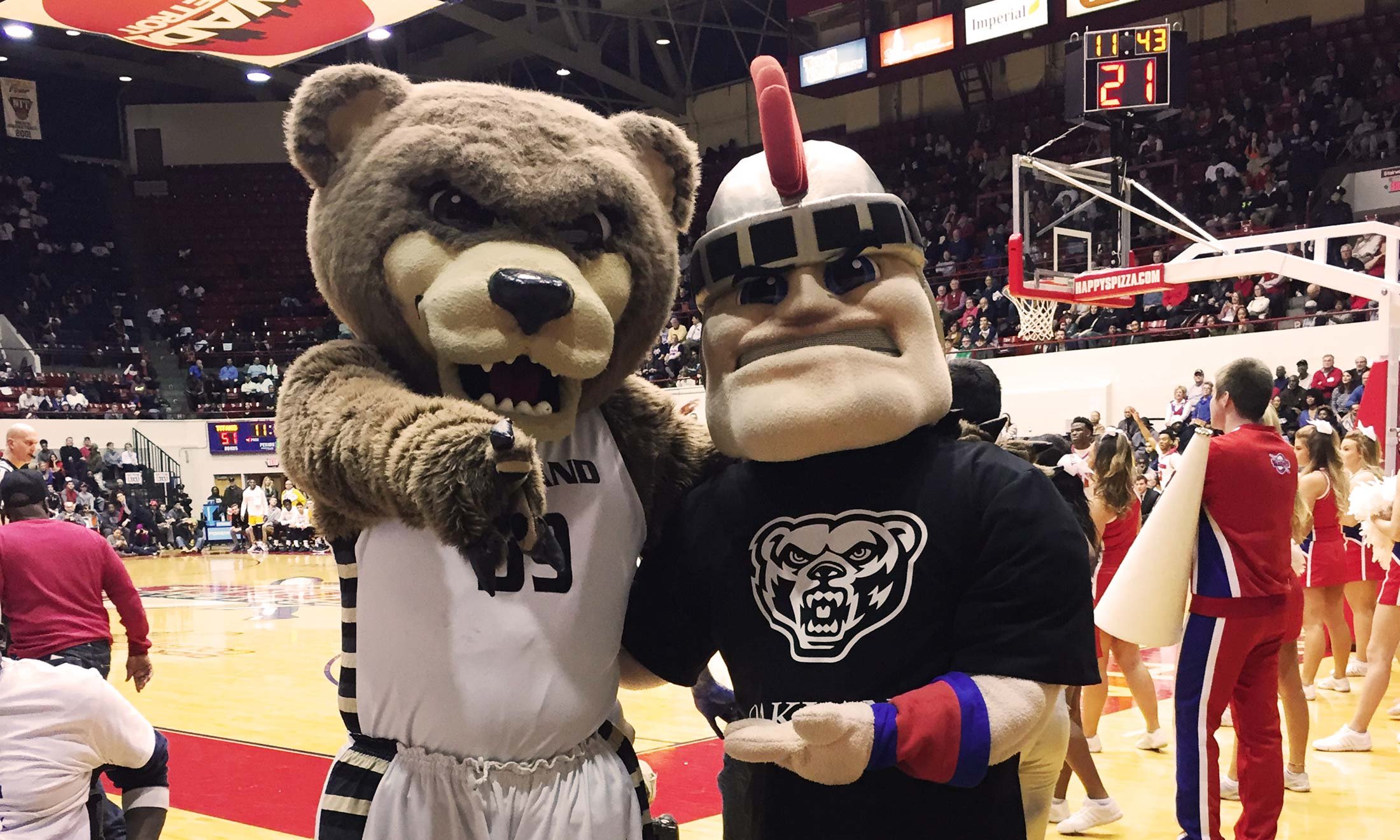 Oakland University's mascot Grizz and Detroit Mercy's mascot Tommy Titan pose together in Calihan Hall. Tommy Titan is wearing an Oakland tshirt.