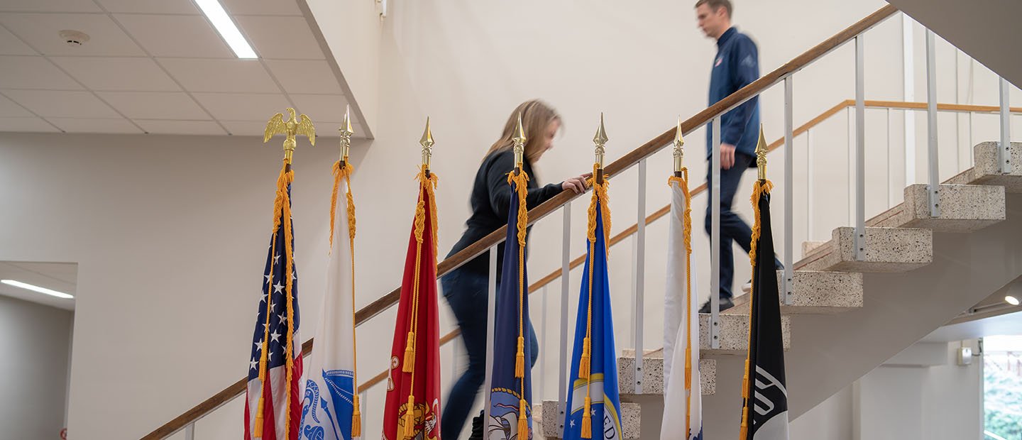 Armed forces flags appear in front of a staircase in a campus building.