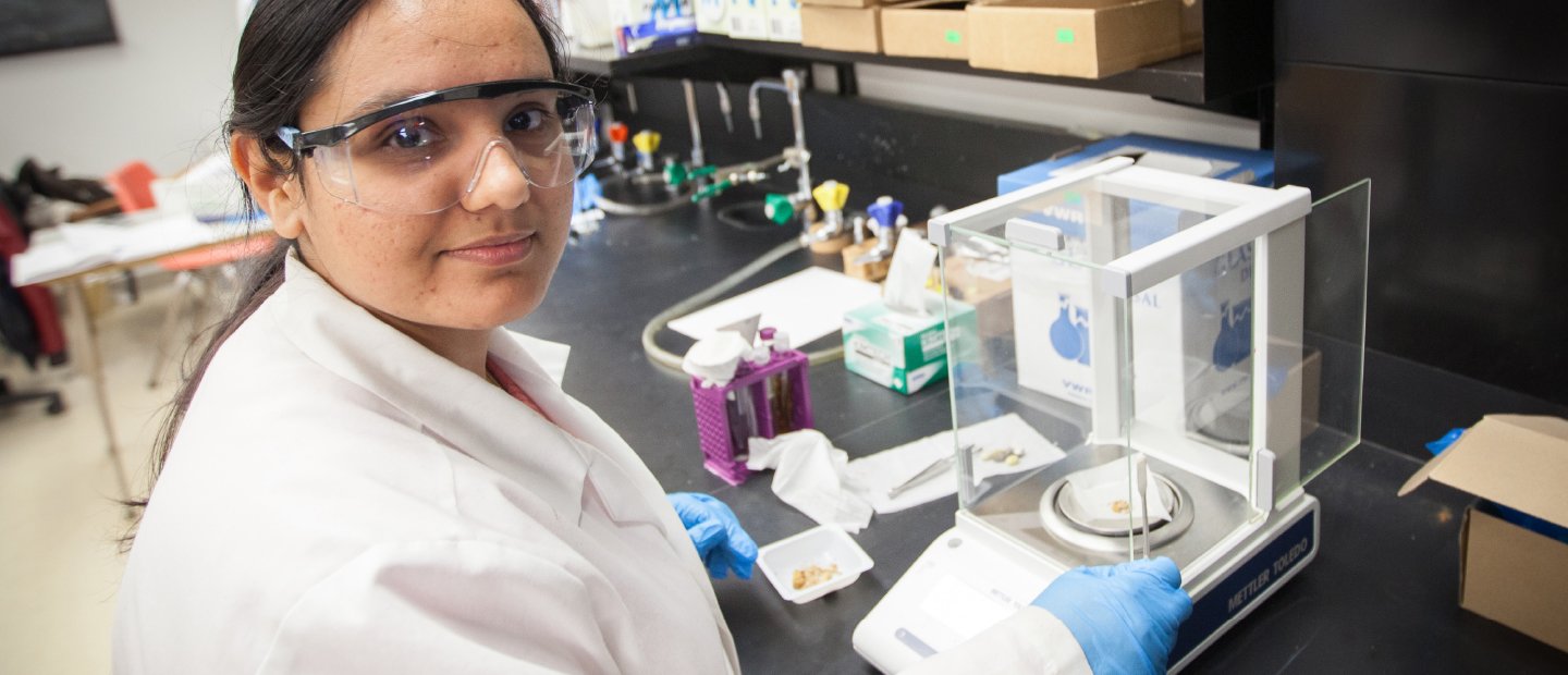 A woman in a lab coat, measuring something on a scale in a lab.