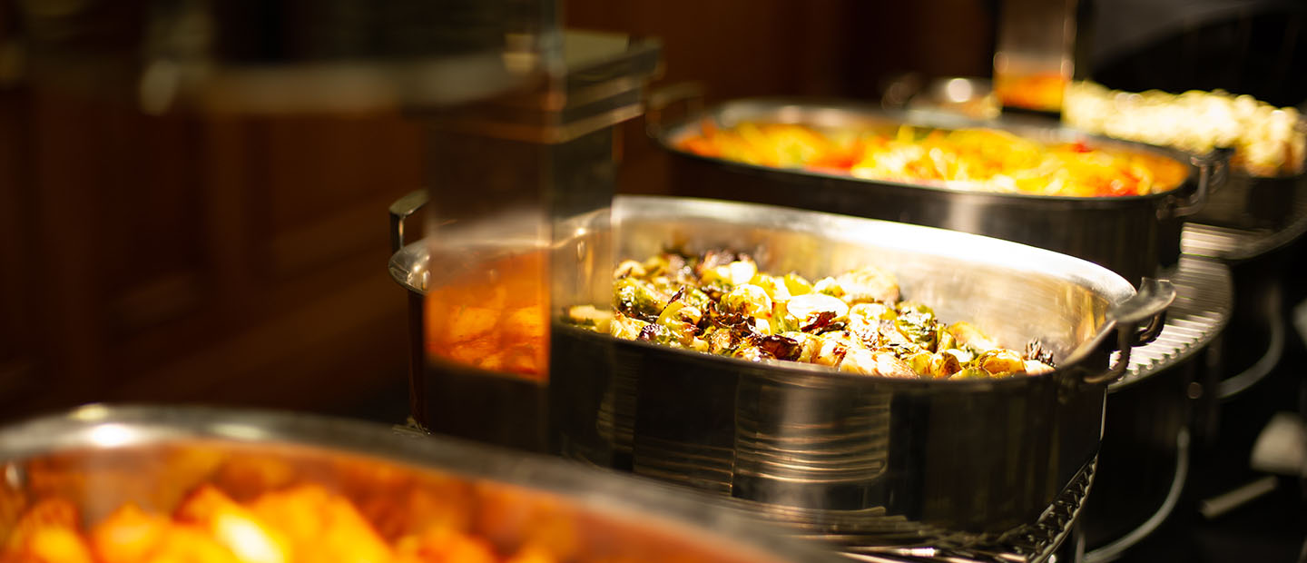 A row of silver dishes full of a variety of catered food.