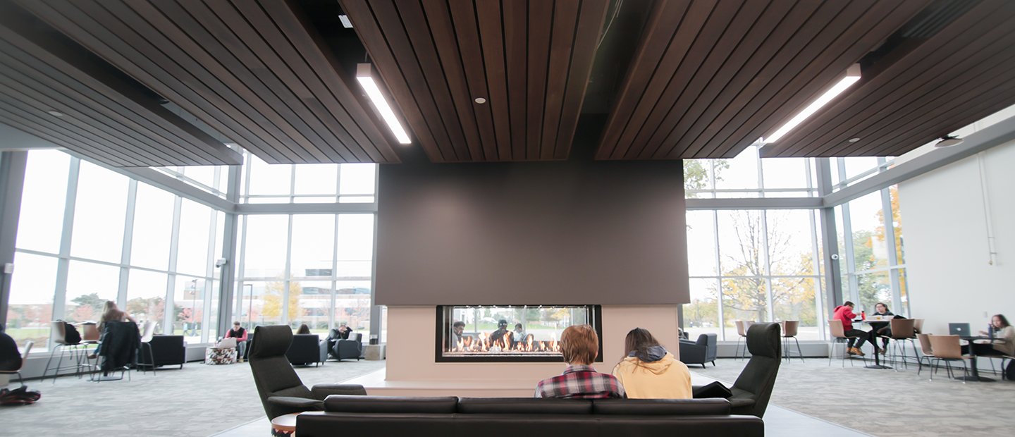 people seated on a couch looking towards a fireplace in the center of a large room