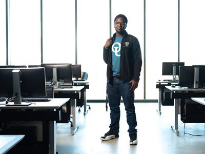 Man in OU tshirt standing in empty computer lab in front of a wall of windows.