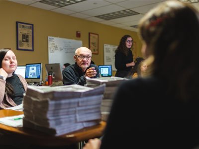 People gathered in discussion around a conference table with tall stacks of paper in the middle of the table