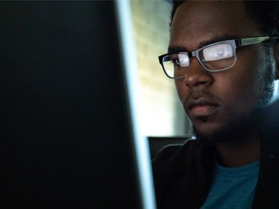 Male student working at a computer, screen reflection can be seen in his eye glasses.