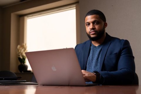 EMBA student, Marcus English, seated at a desk with a laptop, looking at the camera.