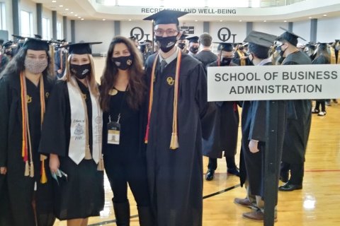 Business Honors Program graduates with Meaghan Cole (adviser), standing next to the School of Business Administration sign at commencement.