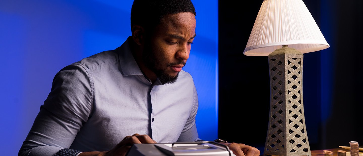 Accounting A man seated at a desk with a lamp, using a large calculator.