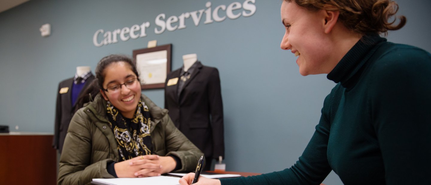 Career Services office visit Women seated across a desk from each other with Career Services on the wall behind them