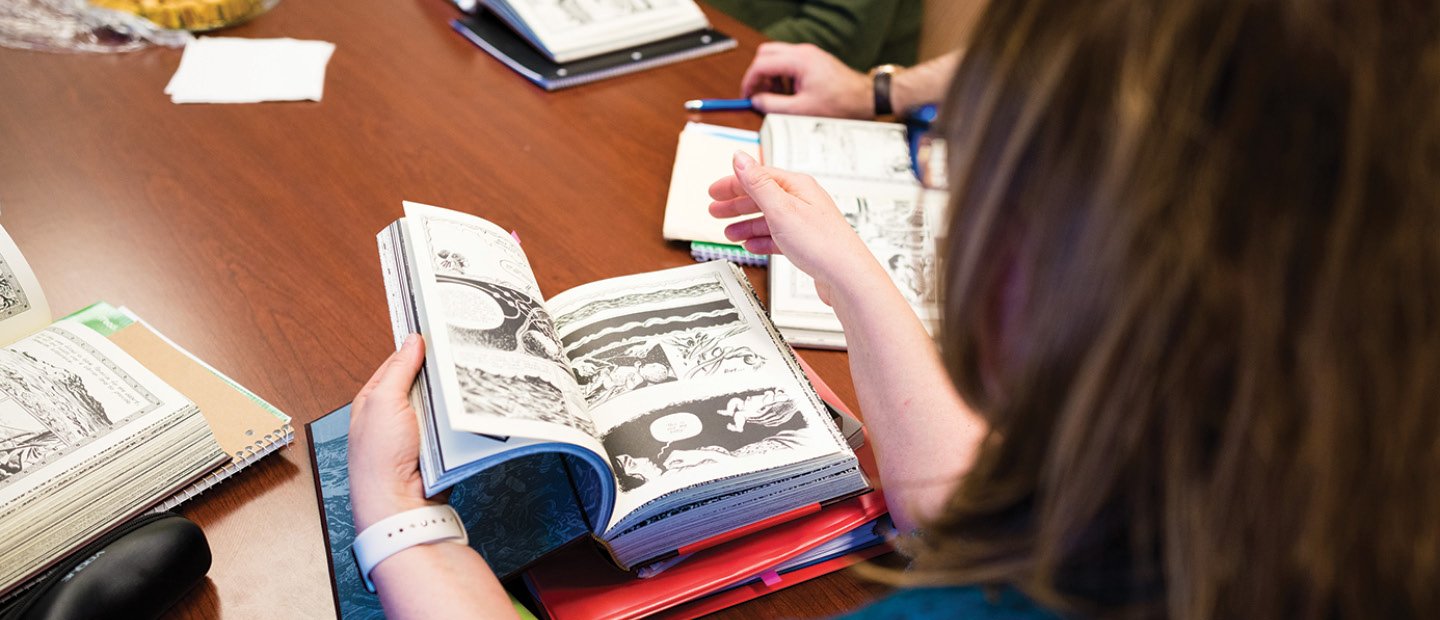 People seated around a table looking at books with illustrations.