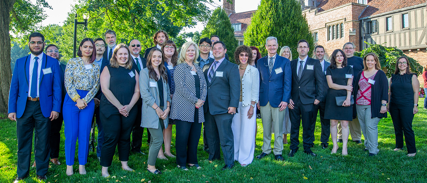 A group photo of Oakland University faculty standing outside of a large brick building.