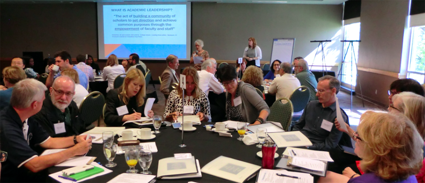 A room full of adults seated at large round tables with notebooks and documents.