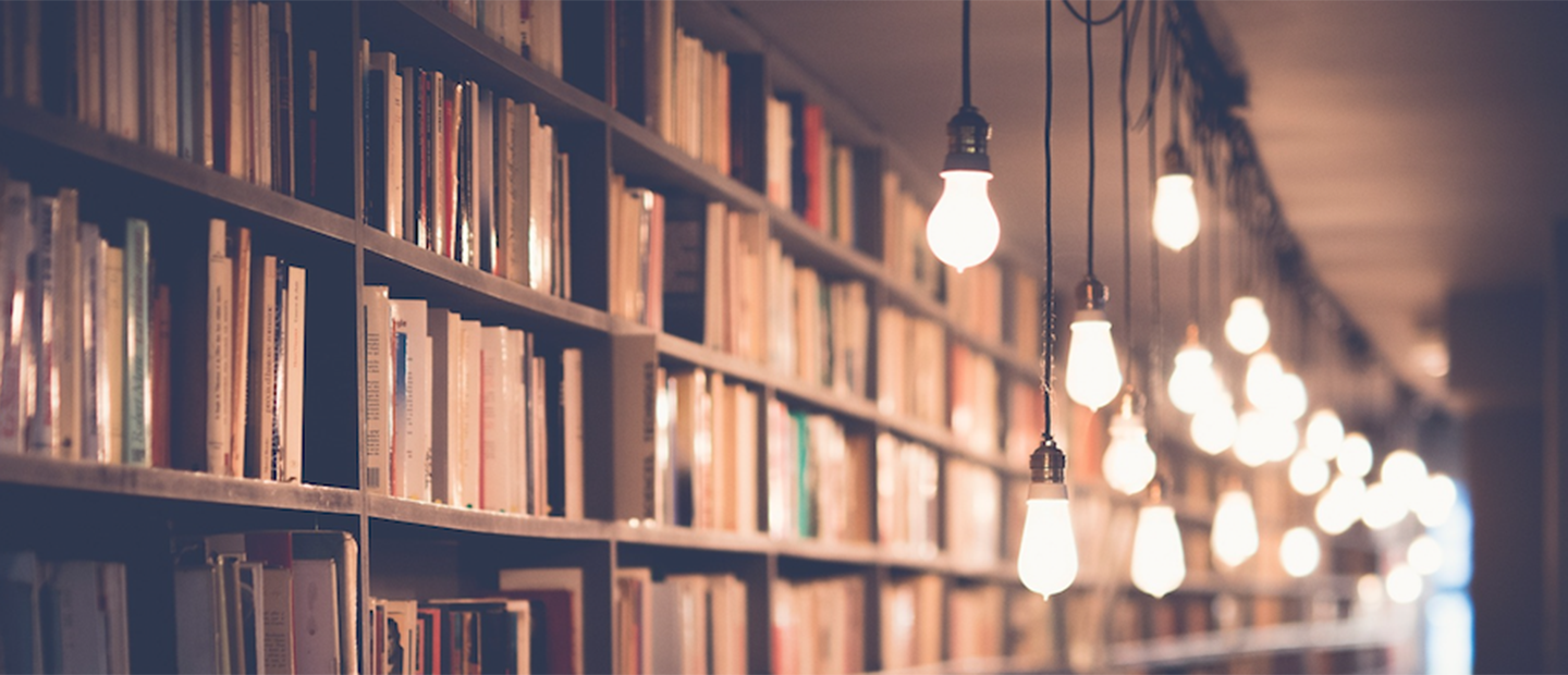 A long row of full bookshelves with hanging lights in front.