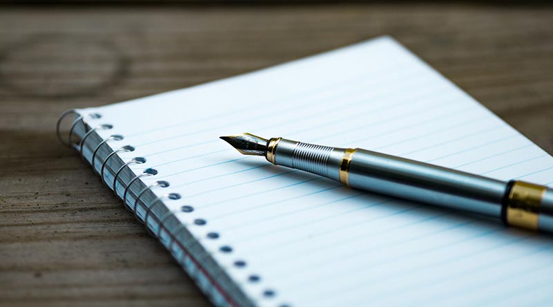 Ink pen laying on a small notebook on a wooden desk