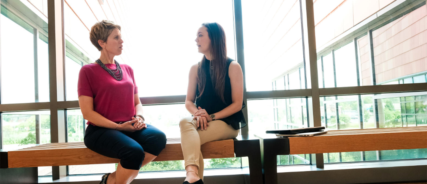 Professor and student sitting on a bench talking at Oakland University.