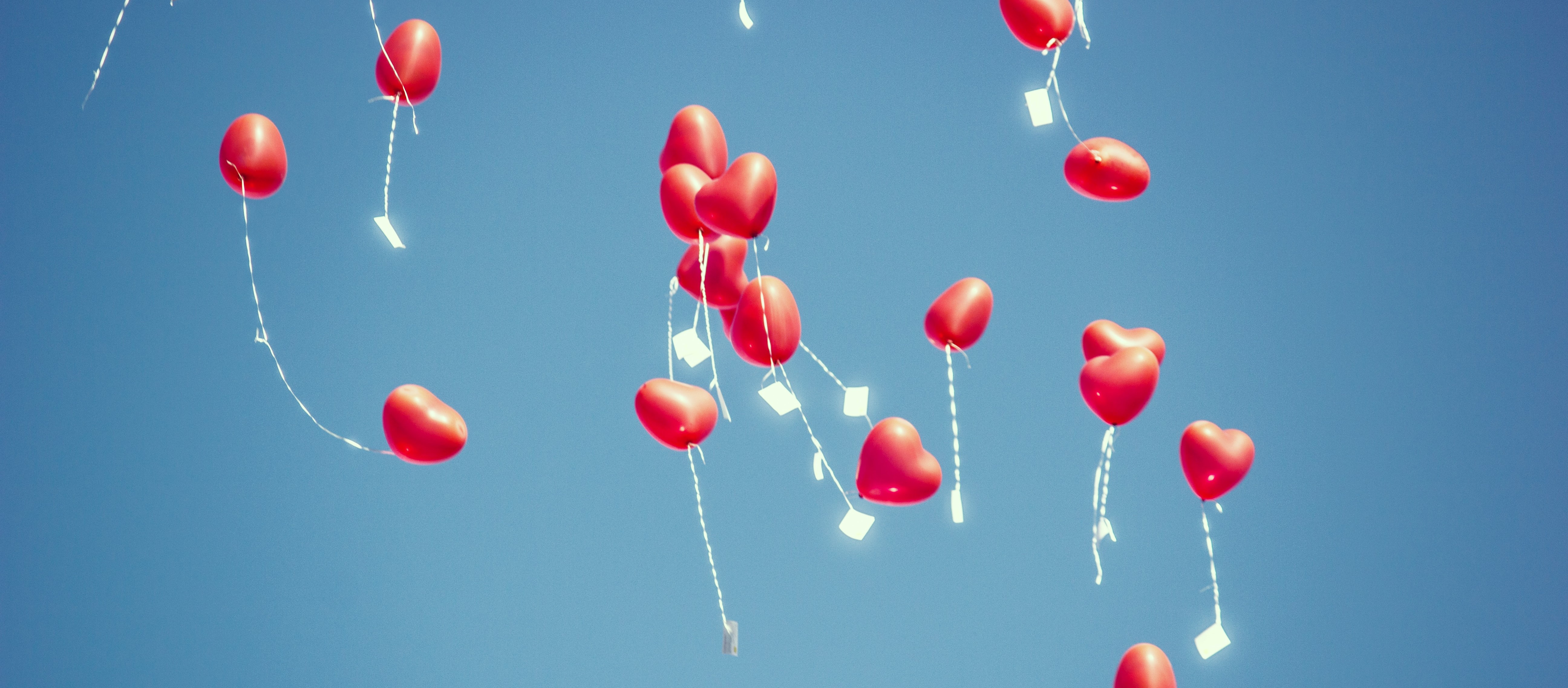 Heart balloons with paper messages attached, floating through the sky