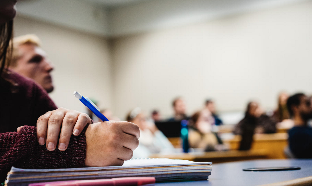 student taking notes with pencil and paper in a classroom