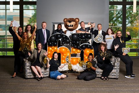 Oakland University Credit Union and Oakland University staff posing for a group photo around a lit up sign that says 65