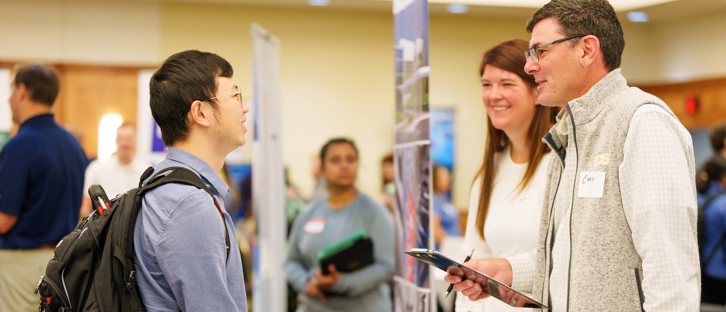 For Students A student talking to employers at a career fair.