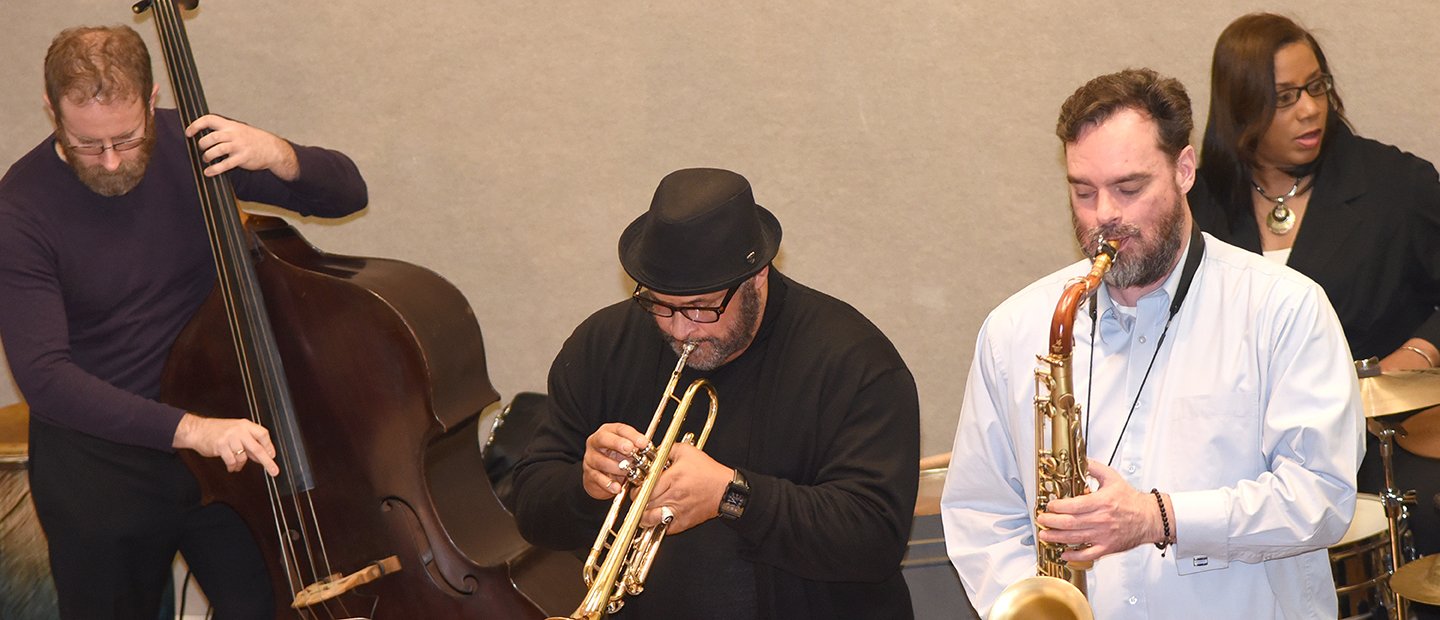 Alumni three men and one woman playing musical instruments