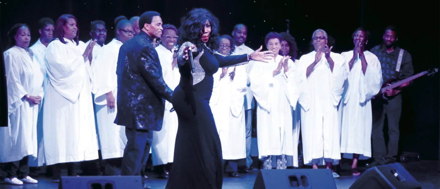 choir of singers in white robes with a woman and man in black in front of them