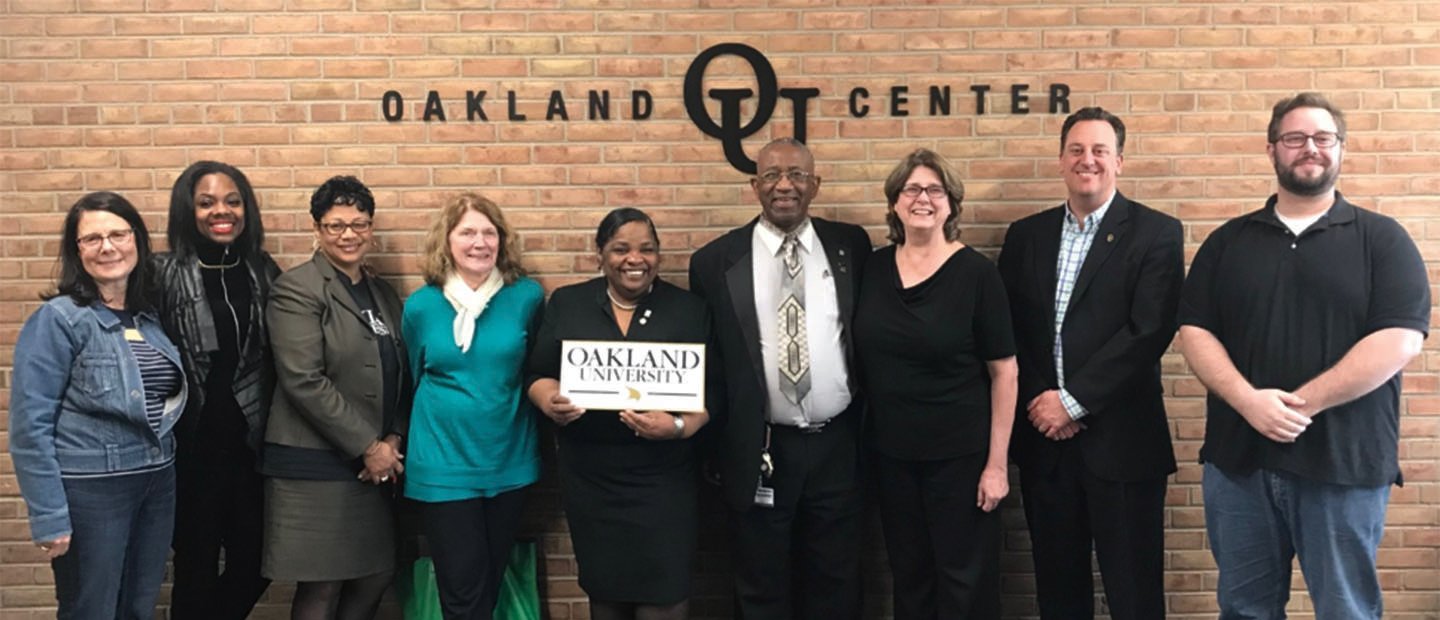 Civic Engagement group of adults posing in front of a wall that says Oakland O U Center