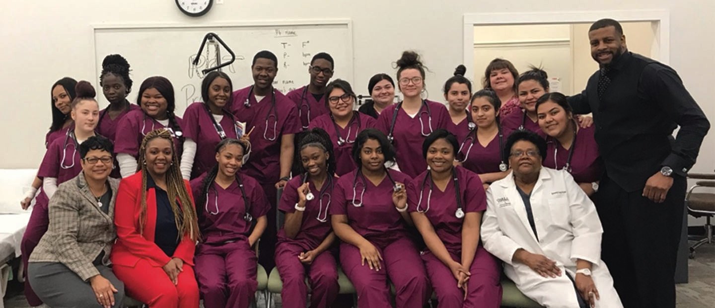 group of students in burgundy scrubs with stethoscopes around their necks, posing with instructors