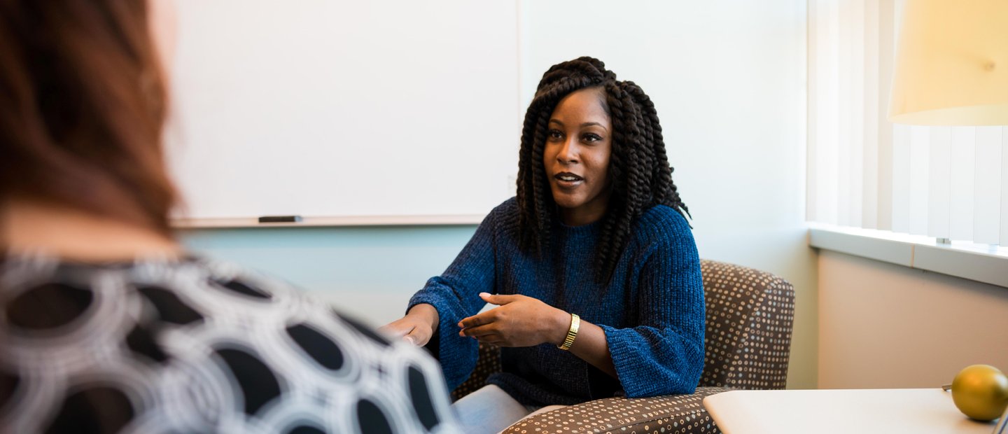 Advising Information A woman seated in an arm chair gesturing with her hands, facing another person.