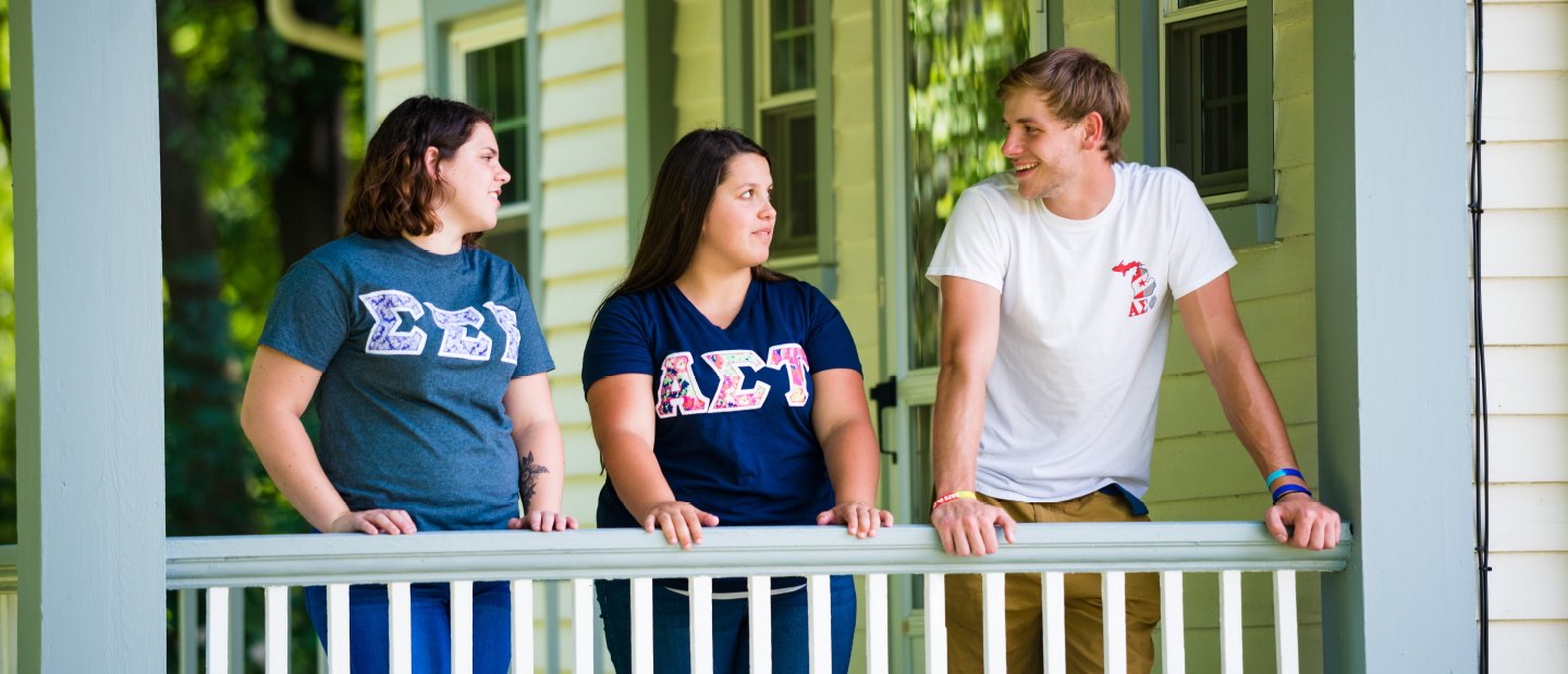 Greek Life students on a porch wearing shirts with Greek letters