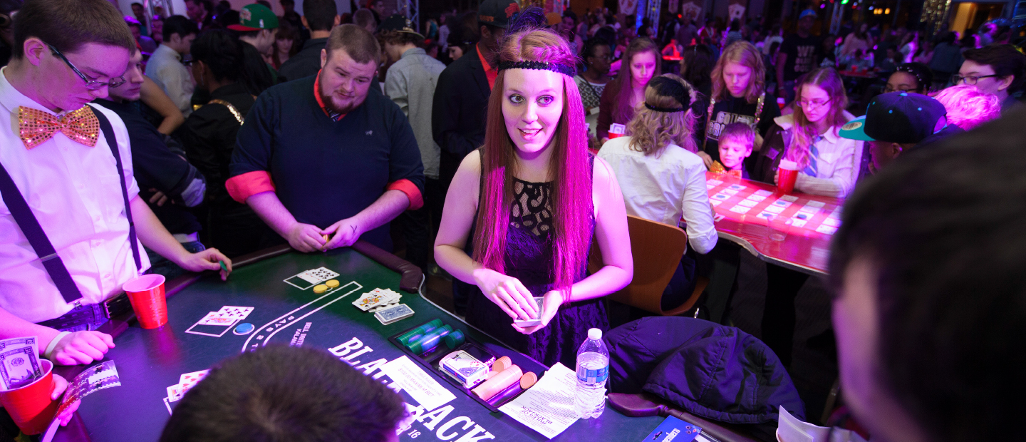 Student Program Board web banner image, a crowded room depicting a casino night, featuring a girl dressed as a flapper dealing cards to a table