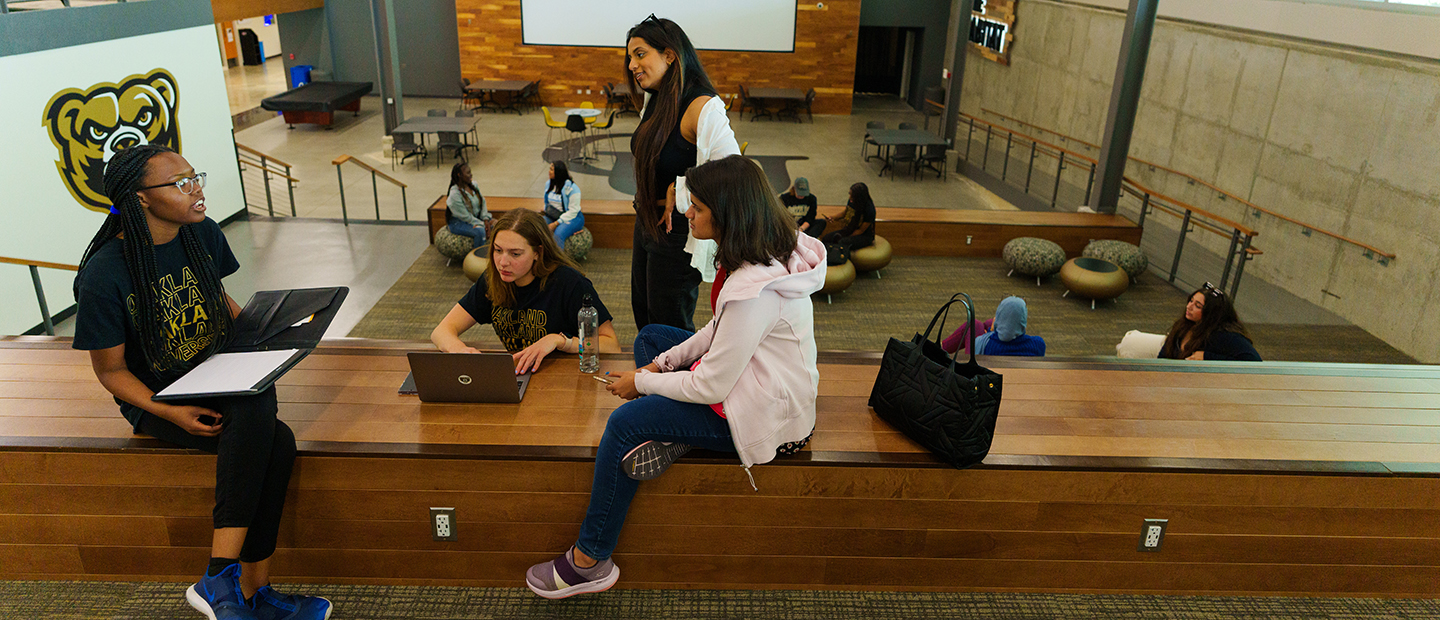 Oakland University students seated together on a ledge in the Oakland Center.