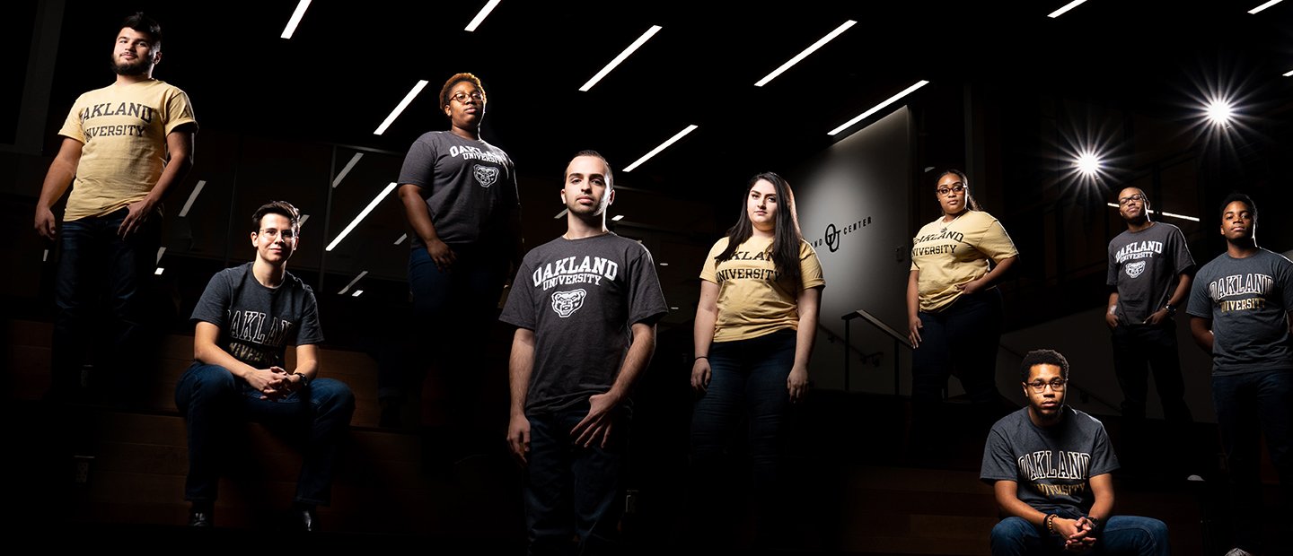 An artistic photo of a group of students, some standing and some sitting, in a dark room with spotlights.