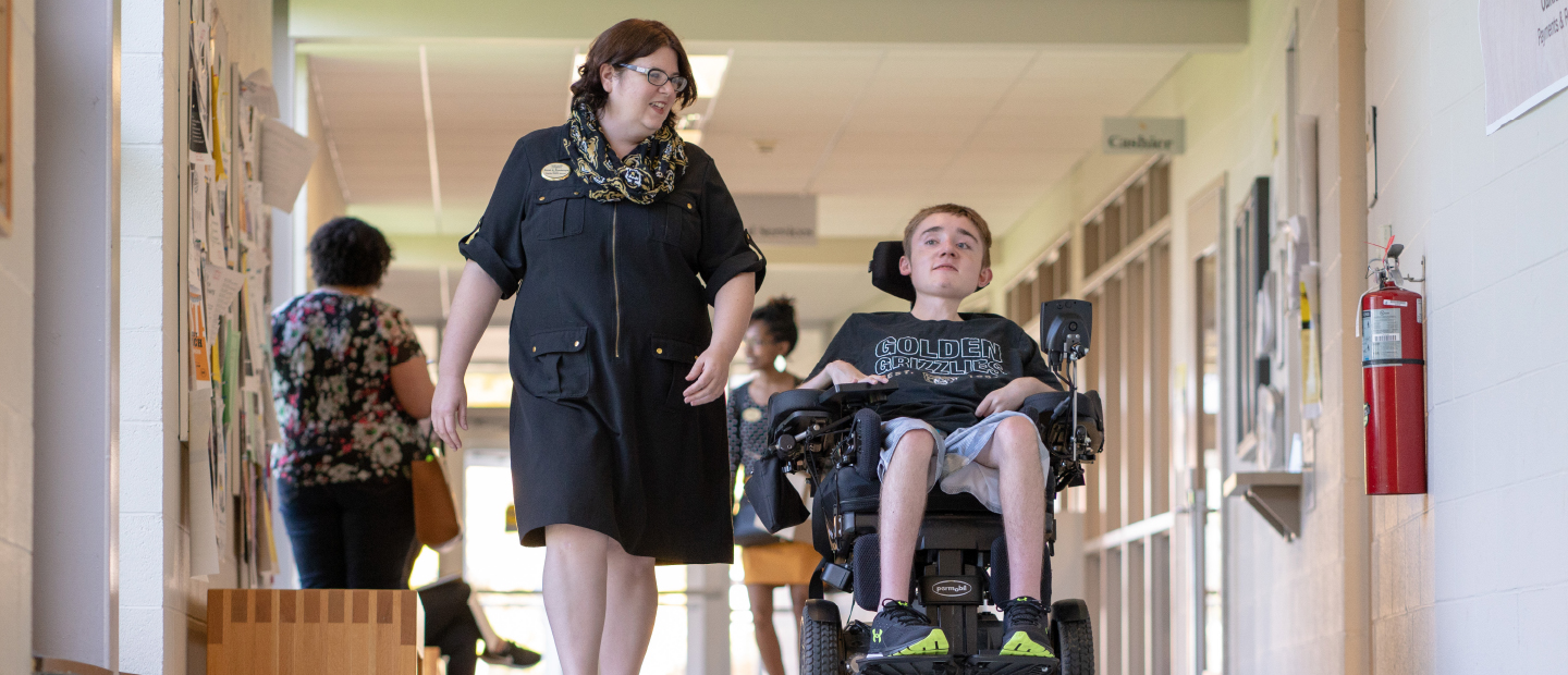 woman walking down a hallway with a young man in a wheelchair next to her