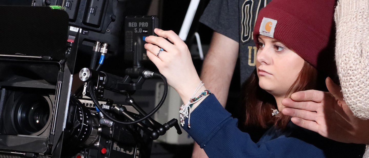 A young woman operating a large video camera.