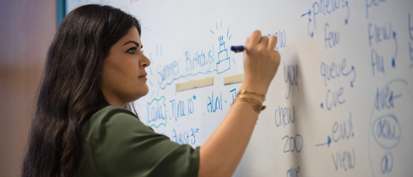 A woman writing on a white board with a blue marker.