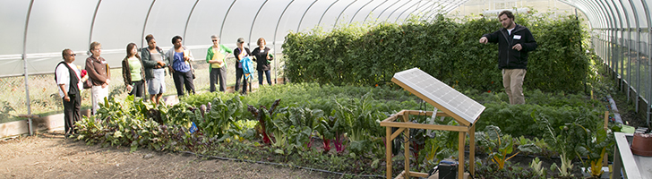 man standing in a greenhouse, pointing at a plant, with a group of students watching him