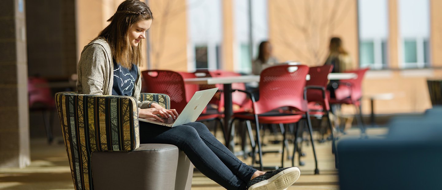 A young woman seated in a chair, typing on a laptop computer.