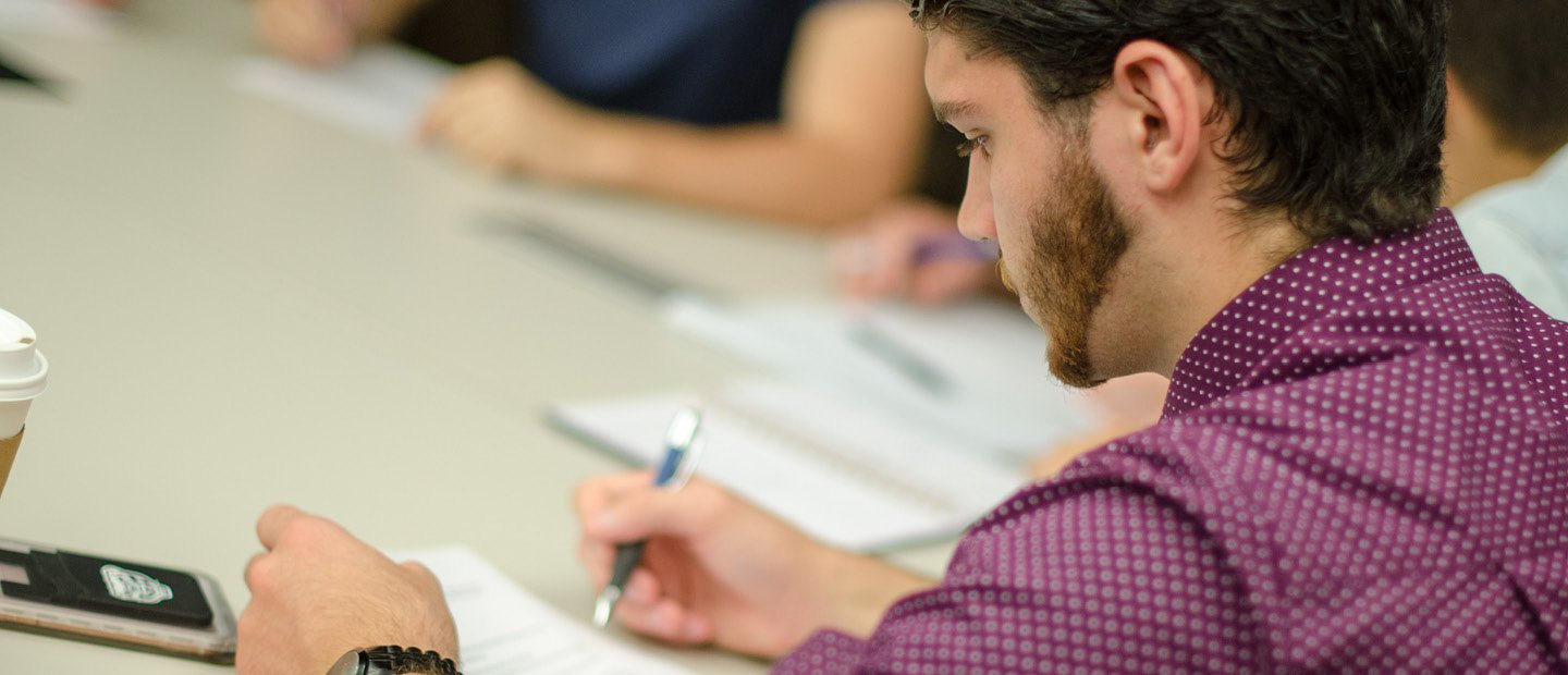 A young man seated at a table, filling out a form.