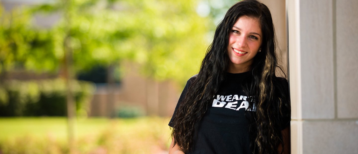 girl in a black t-shirt that ways wear the bear, leaning agains a wall outside