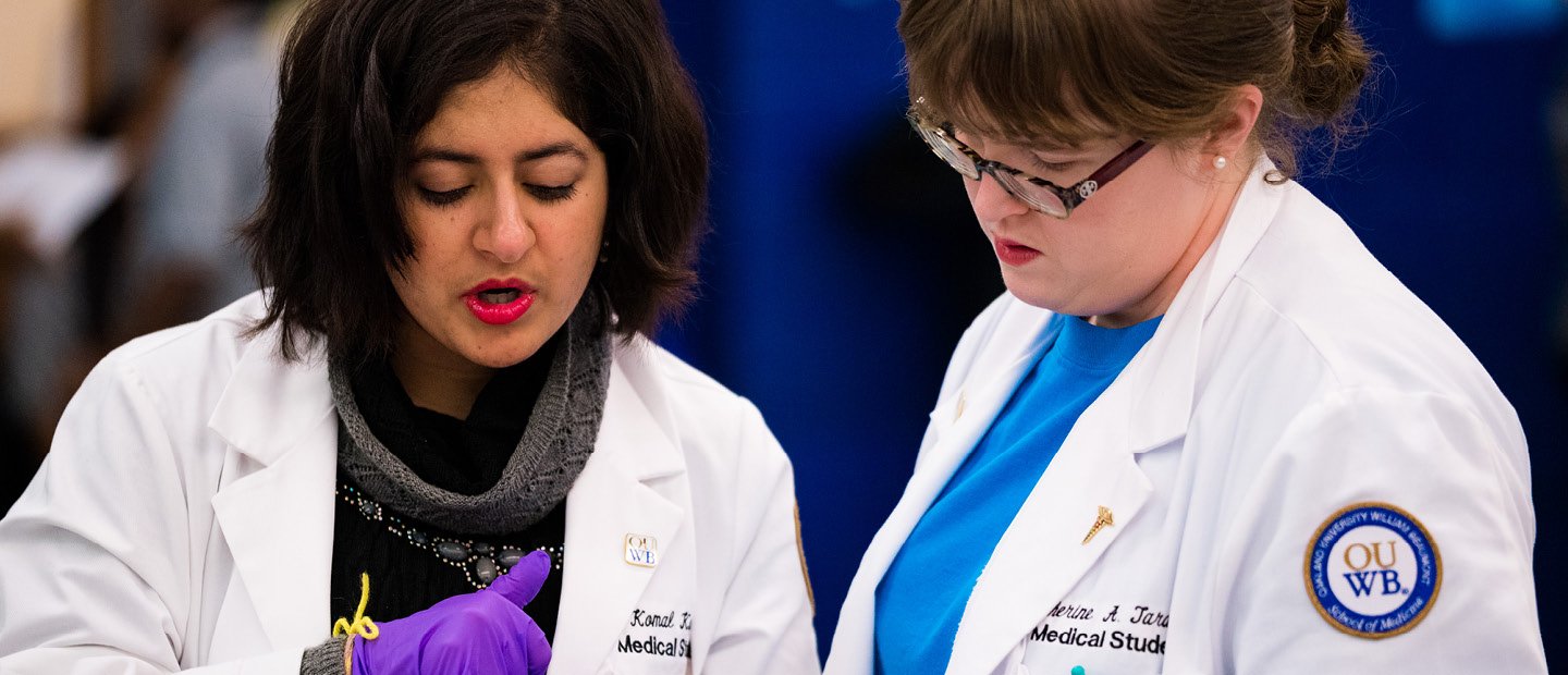 two women wearing white O U W B medical lab coats