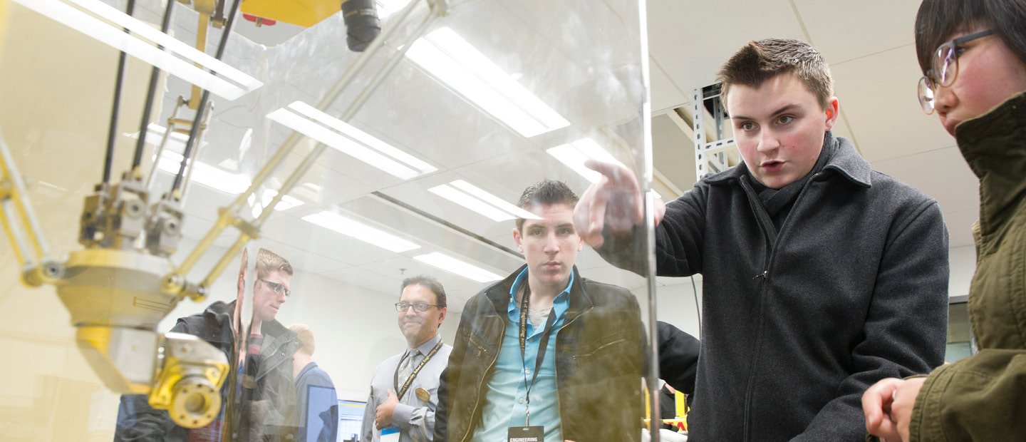 students pointing and looking at a machine in a glass case