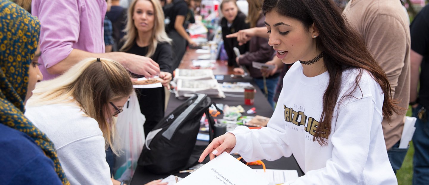 student handing a flyer to a woman at a student organization fair