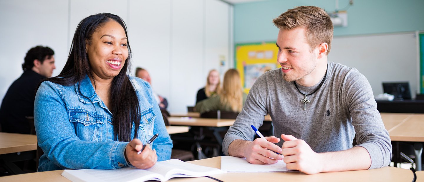 male and female sitting in a classroom at a table with open books