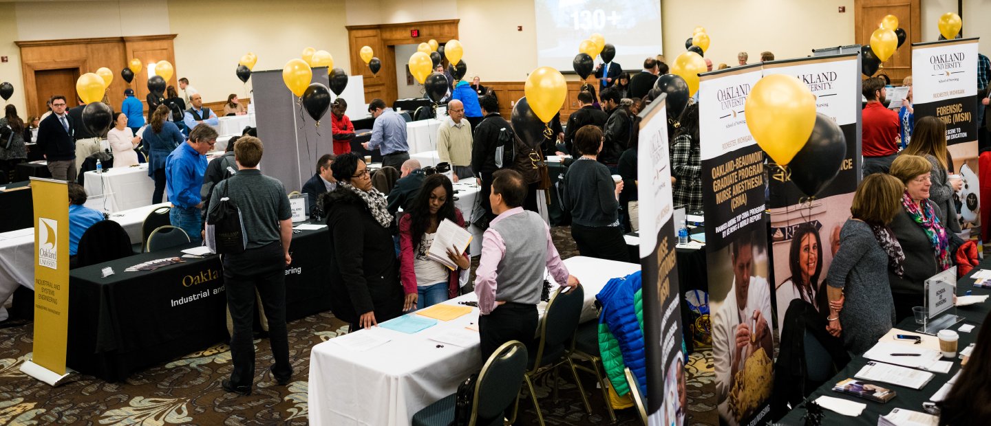 Students at an open house event with display tables, banners and black and gold balloons