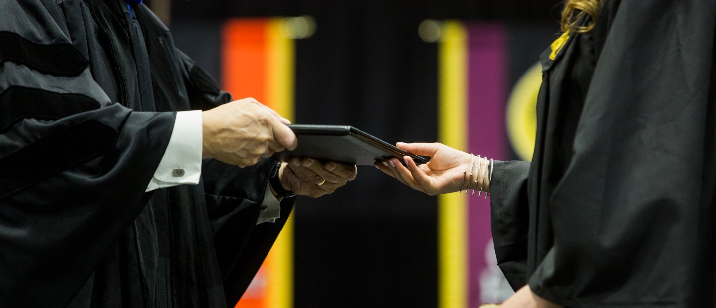 person in a black gown handing a diploma to a student in a black gown