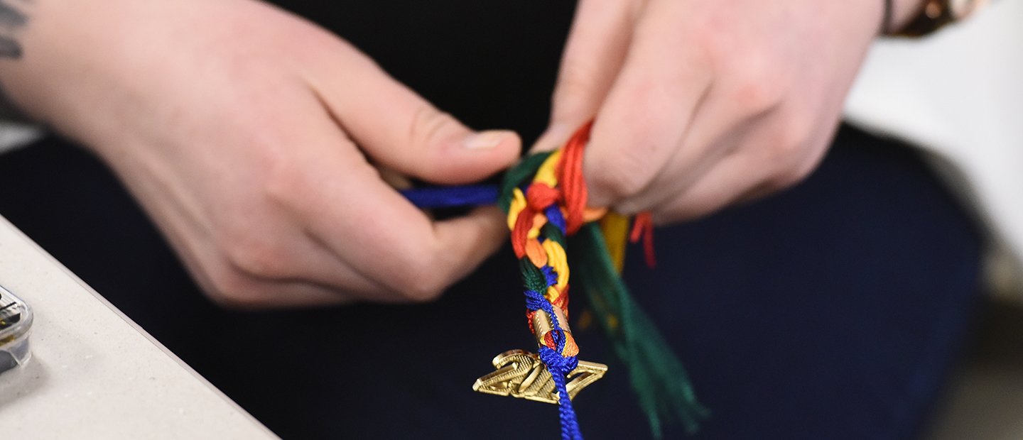 hands braiding a rainbow colored graduation tassle